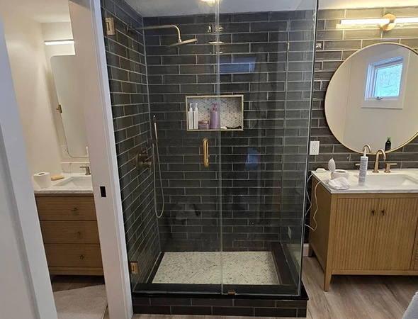 Luxury walk-in shower with dark vertical tiles, gold hardware, and custom built-in shelving by Kennison Construction.