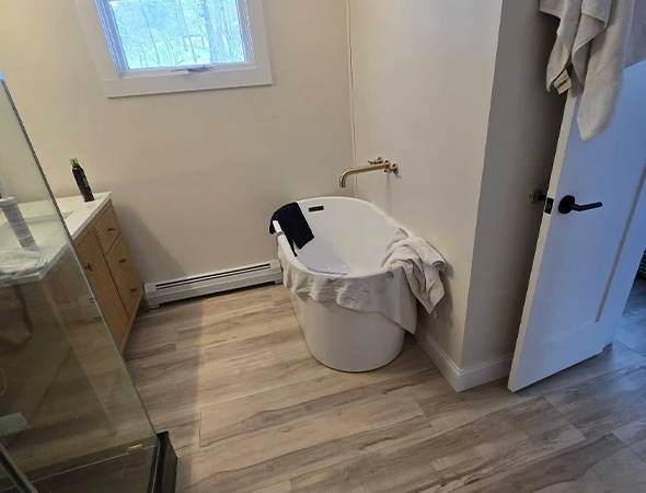 Modern bathroom vanity and sink upgrade in Newport, VT, featuring a light wood cabinet, gold-rimmed circular mirror, and dark tile accent wall.