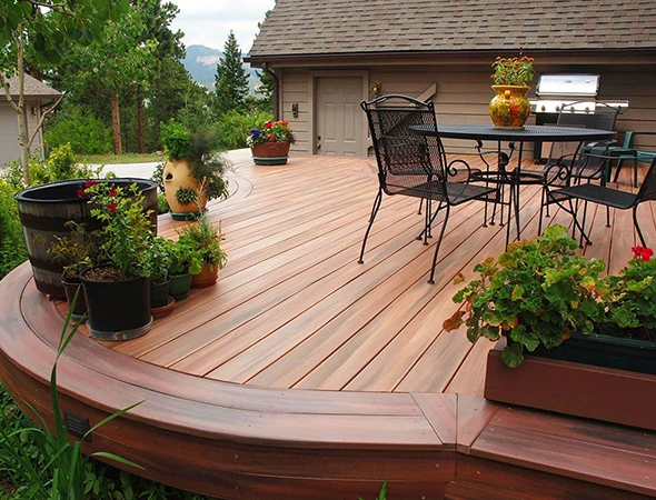 Modern composite curved deck with a black wrought iron patio dining set and decorative potted plants.