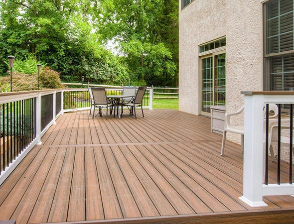 Custom-built composite deck in Montpelier, VT, featuring white railings, a patio dining set, and a sliding glass door entrance overlooking a wooded backyard.