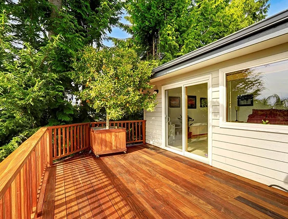 Custom composite deck building in Newport, VT, showing wide wooden stairs with integrated lighting, a patio dining set with an umbrella, and beige vinyl siding.