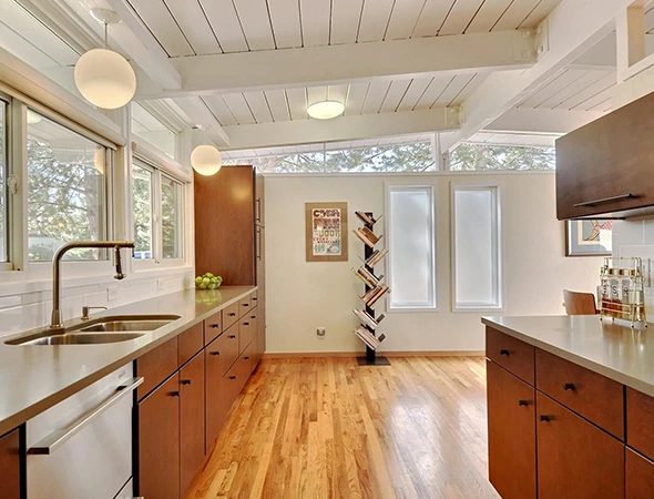 Spacious kitchen remodel in Stowe, VT, featuring natural wood floors, long wood cabinetry, and a bright, open-concept layout with large windows and vaulted ceilings.