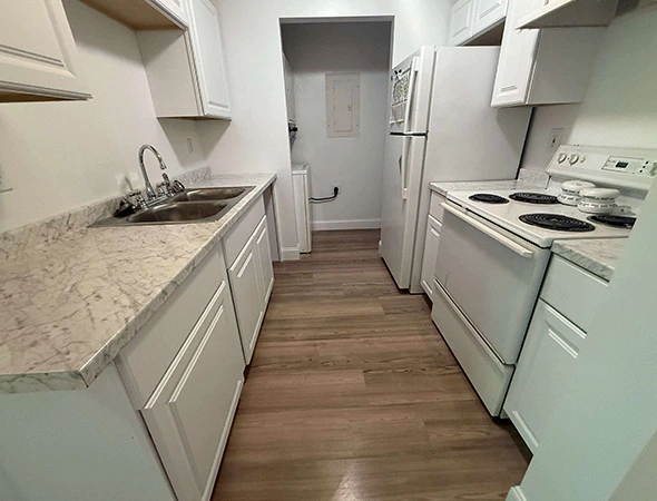 Professional custom white cabinet installation in a Newport, VT galley kitchen with marble-patterned laminate countertops and light wood flooring.