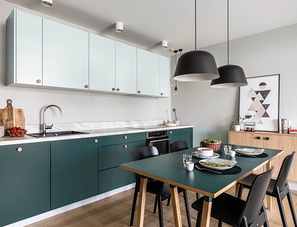 Modern kitchen in Essex, VT featuring dark green lower cabinets, light blue upper cabinets, and durable quartz countertops with a matching dining table.