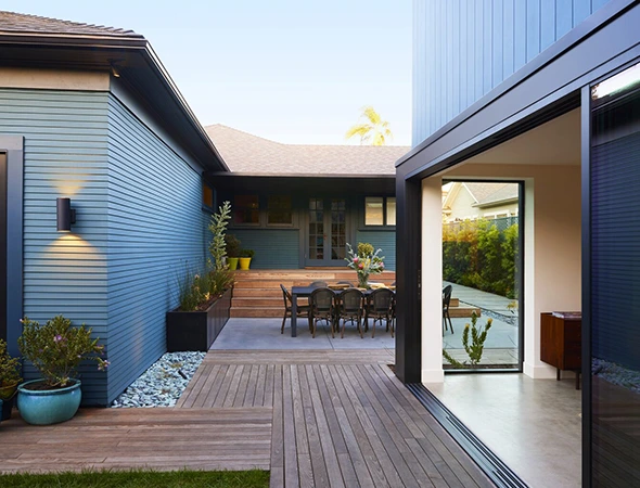 Modern blue horizontal siding home addition in Stowe, VT, featuring a spacious wooden deck and outdoor dining area.
