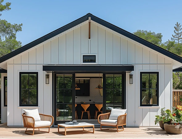 White modern farmhouse style home expansion with black-trimmed sliding glass doors and a sun-lit patio area in Burlington, VT.