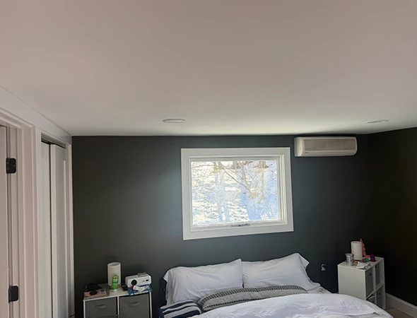 Renovated bedroom in Burlington featuring a dark grey accent wall, white ceiling, new window installation, and wall-mounted AC unit.