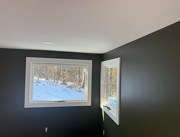Modern interior renovation in Stowe, VT, featuring dark charcoal accent walls, white-trimmed windows with a snowy outdoor view, and a clean white ceiling.